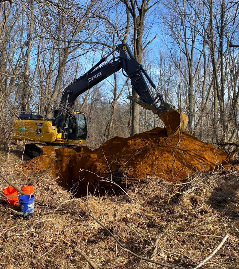 A small excavator digging in a forest for geotechnical investigations