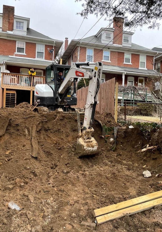 An excavator digging deep in someone's town home backyard